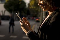 Улыбающаяся деловая женщина с мобильного телефона на улице в вечерние сумерки, частичный вид — стоковое фото