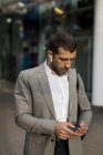 Businessman with cell phone and bluetooth earbuds in the city — Stock Photo