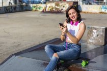 Ritratto di giovane donna sorridente con cuffie e cellulare in uno skatepark — Foto stock