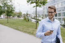 Young businessman walking in park, using smartphone — Stock Photo