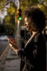 Улыбающаяся деловая женщина, использующая мобильный телефон на улице в вечерние сумерки — стоковое фото