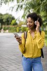 Улыбающаяся женщина слушает музыку в наушниках и смартфонах на открытом воздухе — стоковое фото