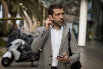 Businessman with cell phone in the city applying earbuds — Stock Photo