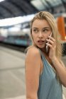 Portrait de jeune femme sur téléphone portable à la gare regardant autour — Photo de stock