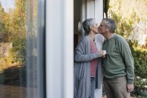 Cariñosa pareja mayor besándose en la puerta de la terraza - foto de stock