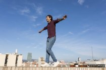 Hombre en una terraza en la azotea, balanceándose en una pared - foto de stock
