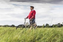 Старший чоловік з велосипедом у сільському пейзажі — стокове фото