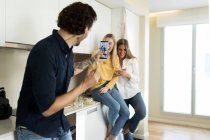 Amigos se divertindo de pé na cozinha, tirando fotos com seus smartphones — Fotografia de Stock