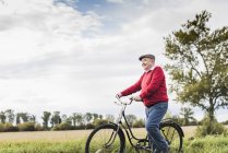 Hombre mayor empujando bicicleta en el paisaje rural - foto de stock