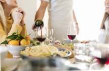 Amici che pranzano insieme, ospiti che versano vino rosso — Foto stock