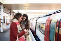 Royaume-Uni, Londres, deux femmes utilisant un téléphone portable au quai de la station de métro — Photo de stock