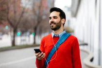 Casual businessman commuiting in the city, using earphones and smartphone — Stock Photo