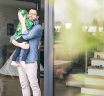 Pai afetuoso carregando filho em um traje na porta do terraço em casa — Fotografia de Stock