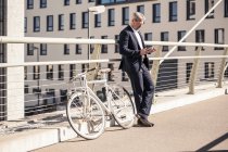 Hombre de negocios maduro con bicicleta usando el teléfono celular en la ciudad - foto de stock