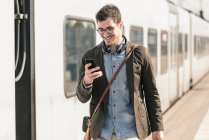 Lächelnder junger Mann mit Handy am Bahnsteig — Stockfoto