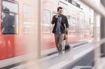 Lächelnder junger Mann mit Handy läuft auf S-Bahn-Bahnsteig — Stockfoto