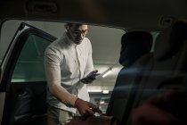 Hombre joven con teléfono celular y auriculares sacando el bolso del coche - foto de stock