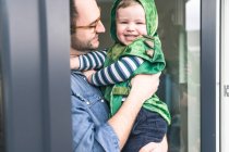 Pai carregando filho feliz em um traje na porta do terraço em casa — Fotografia de Stock