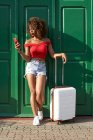 Woman in red with a suitcase checking her phone — Stock Photo