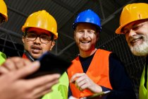 Happy workers in factory warehouse talking and using tablet — Stock Photo