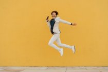 Felice uomo d'affari che salta in aria davanti al muro giallo ascoltando musica con le cuffie — Foto stock