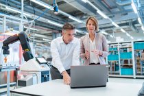 Businessman and businesswoman with laptop talking in a modern factory hall — Stock Photo