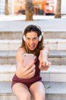 Young woman using smartphone and listening music, taking a selfie — Stock Photo