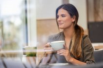 Junge Geschäftsfrau mit Kaffeetasse in einem Café, aus dem Fenster gesehen — Stockfoto