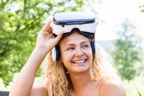 Young blond woman using virtual reality glasses outdoors, looking sideways — Stock Photo