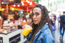 Portrait of young woman drinking fresh orange juice on street market, London, UK — Stock Photo