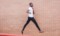 Young man wearing white t-shirt jumping at a brick wall — Stock Photo