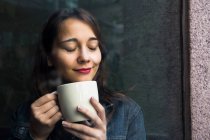 Jeune femme dans un café avec une tasse de café et les yeux fermés — Photo de stock
