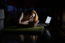 Young woman using laptop and cell phone late at night — Stock Photo