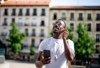 Smiling young man using smartphone and ear phones, looking up — Stock Photo