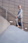 Fashionable mature businessman with bag walking up stairs — Stock Photo