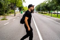 Молодий чоловік з рюкзаком, що переходить вулицю в місті — стокове фото