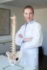 Portrait of confident female doctor in medical practice with spine column — Stock Photo
