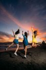 Vista posteriore di tre amiche spensierate che saltano sulla spiaggia al tramonto — Foto stock