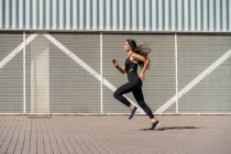 Jovem jogger feminino correndo na frente de uma parede — Fotografia de Stock