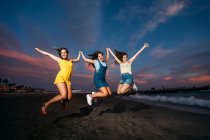 Tre amiche spensierate che saltano sulla spiaggia al tramonto — Foto stock