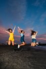 Tre amiche spensierate che saltano sulla spiaggia al tramonto — Foto stock