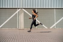 Jovem jogger feminino correndo na frente de uma parede — Fotografia de Stock