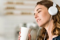 Jeune femme dans un café écouter de la musique avec des écouteurs — Photo de stock