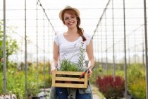 Ritratto di bella giovane donna che tiene la scatola di legno con le piante nella serra — Foto stock