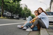 Amigos do sexo feminino sentados na beira da estrada na cidade — Fotografia de Stock