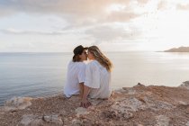 Visão traseira do jovem casal apaixonado sentado na rocha em frente ao mar, Ibiza, Ilhas Baleares, Espanha — Fotografia de Stock
