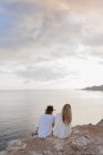 Visão traseira do jovem casal sentado na rocha em frente ao mar, Ibiza, Ilhas Baleares, Espanha — Fotografia de Stock
