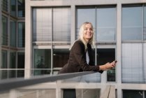 Blond businesswoman using smartphone in the background modern buildings — Stock Photo