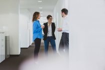 Empresario y dos empresarias tomando un café hablando en el pasillo de la oficina - foto de stock