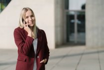 Blond businesswoman using smartphone, looking at camera — Stock Photo